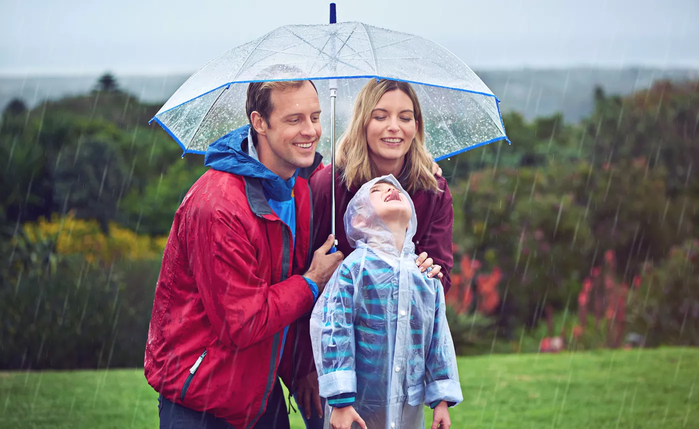  A young family stands together in the rain, smiling under an umbrella.
