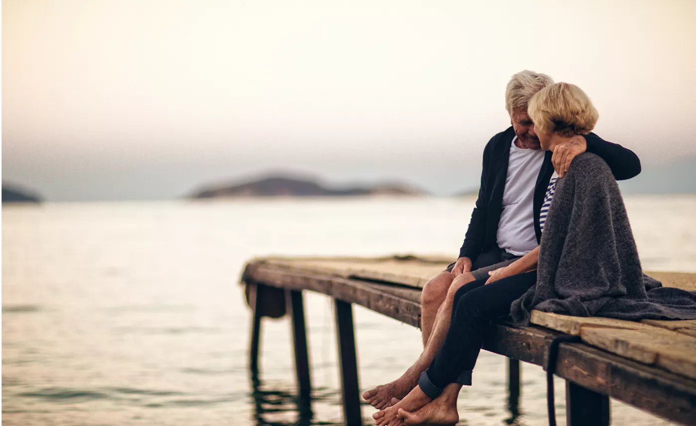  A senior couple sit together on a dock.
