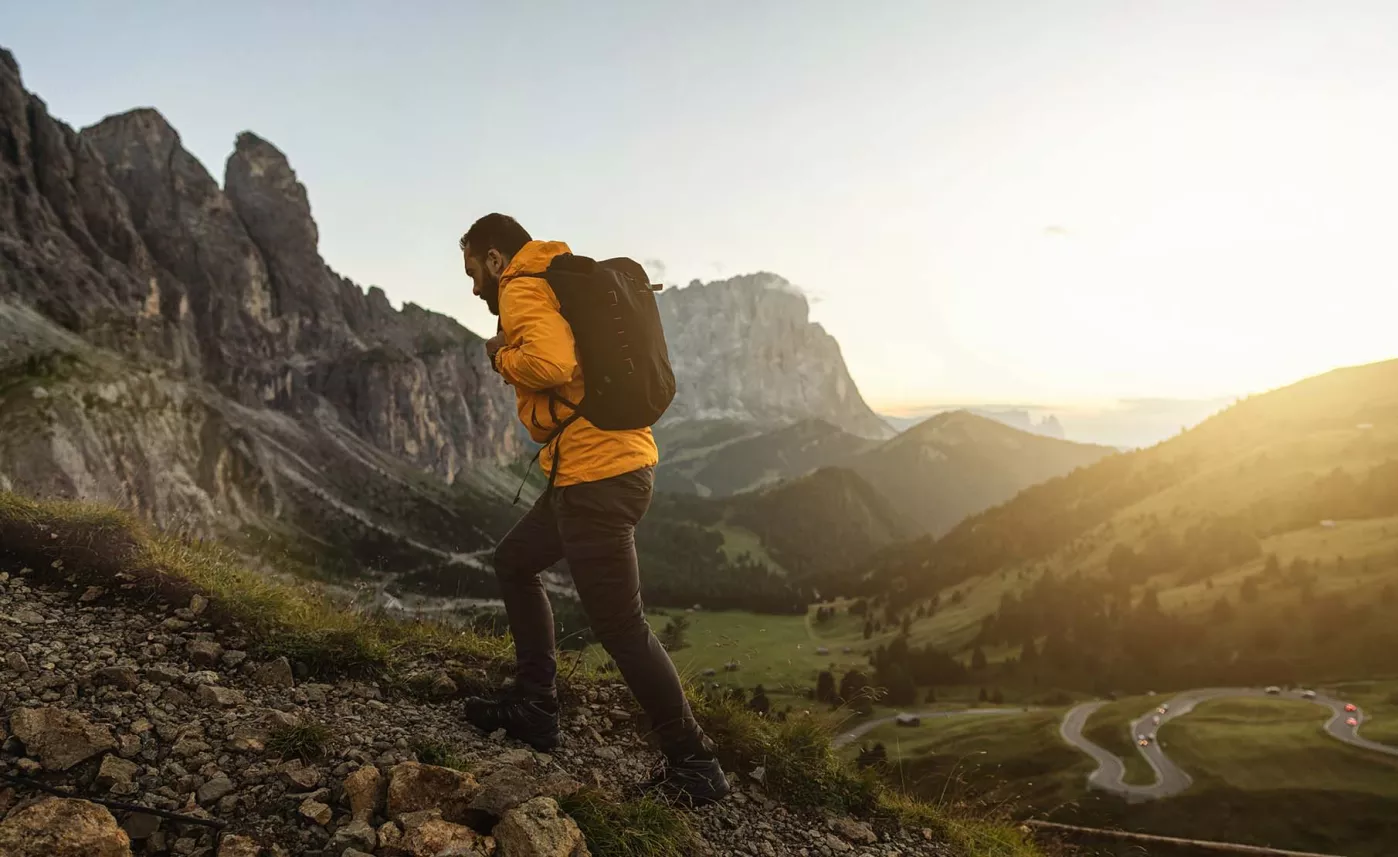  Man in a yellow jacket with backpack going up a mountain

