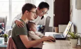 Young parents look up information on their laptop with a small infant on the father's lap.