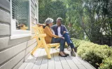 A senior couple smiles at each other on their porch on a sunny day.